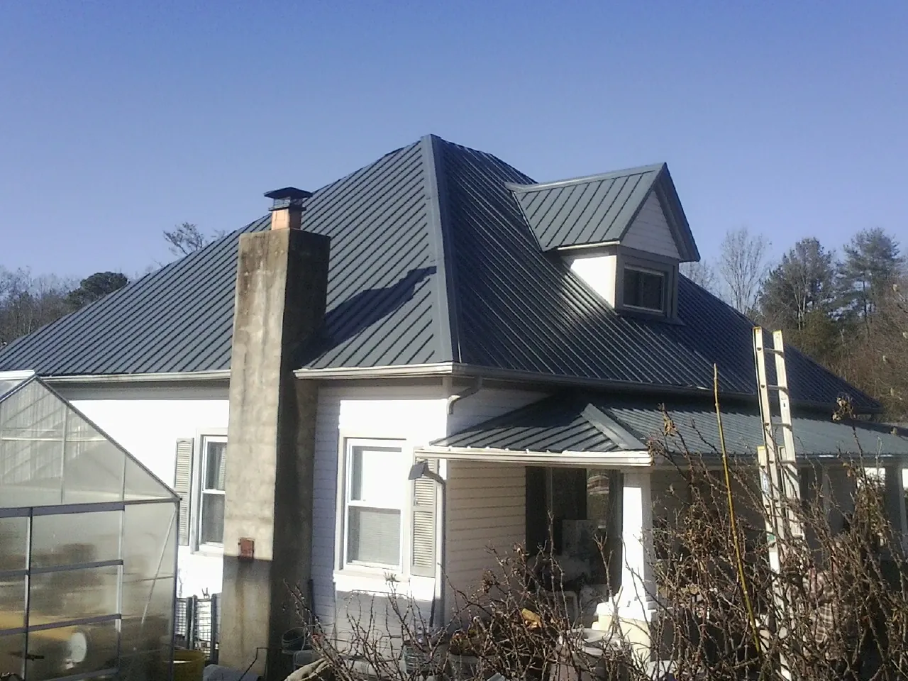 Dark blue standing seam metal roof on a white farmhouse with dormer — Slate & Tile Roof Repair by Roofing Brothers in Blaine