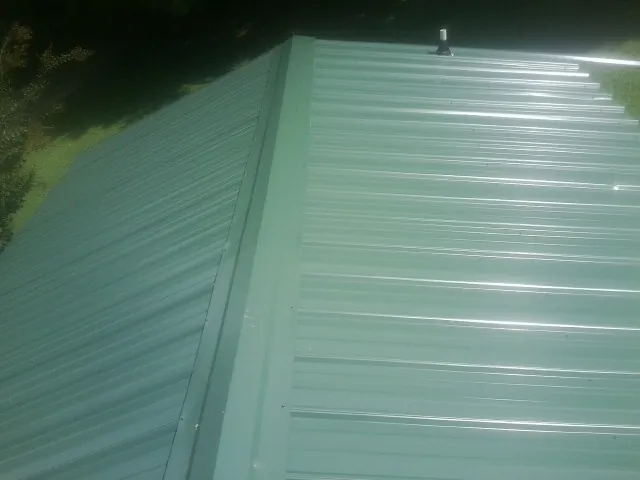 New green metal panels meeting at the ridge of a roof — Flat Roof Repair work by our crew in Blaine