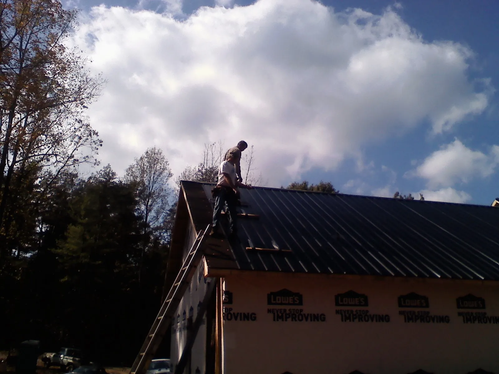 Roofer fastening dark metal panels high against a cloudy sky, from a Roof Inspection job in Blaine