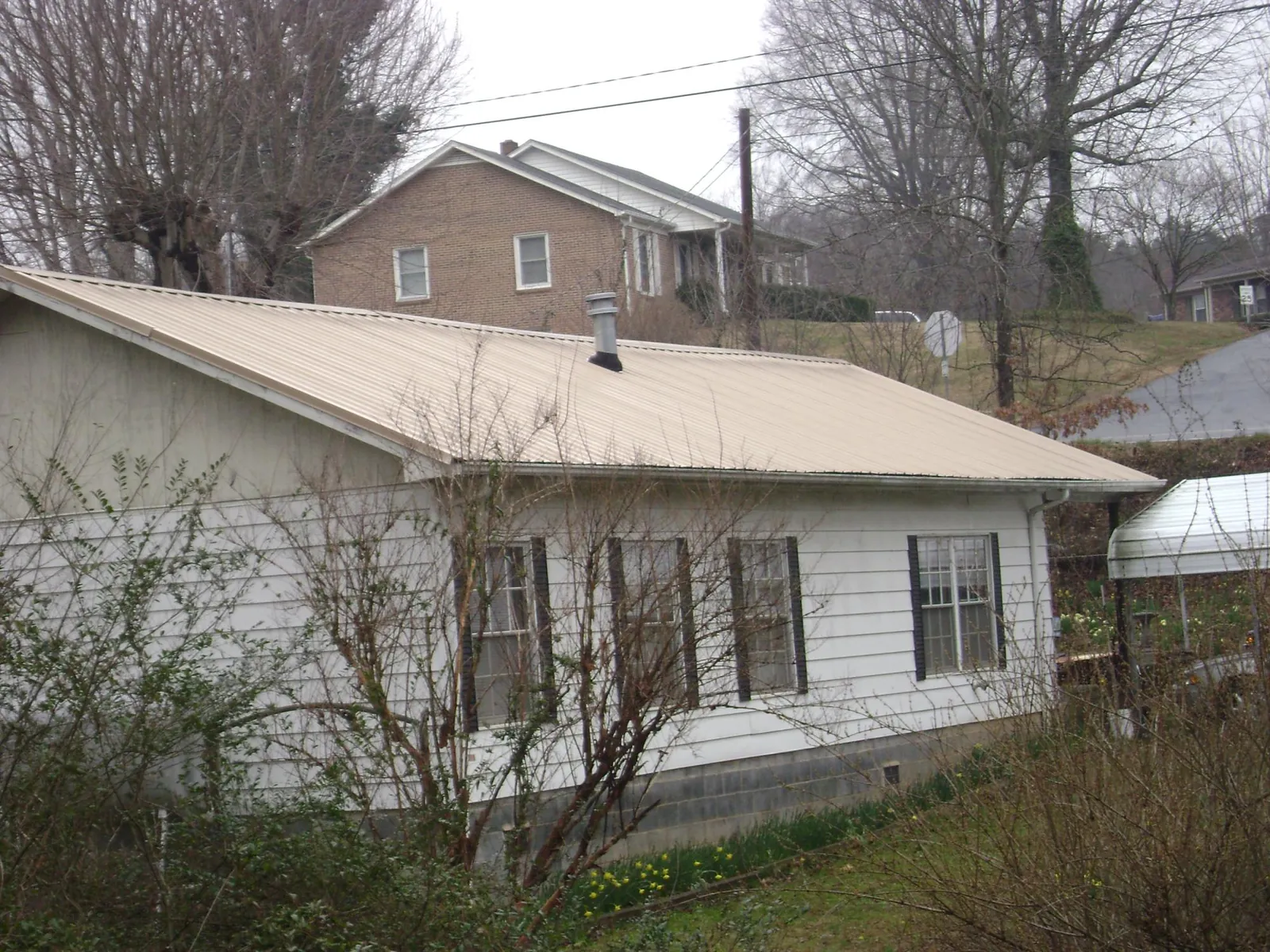 Tan metal roof on a white sided house set into a hillside — Commercial Roofing by Roofing Brothers in Blaine